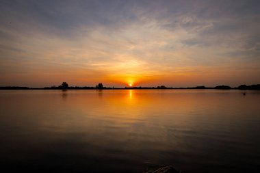 Akşamları güzel günbatımının manzarası gölün üzerinde, gölün üzerinde siluet suyun üzerinde ve bulutların sakin sularda yansıması.