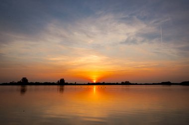 Akşamları güzel günbatımının manzarası gölün üzerinde, gölün üzerinde siluet suyun üzerinde ve bulutların sakin sularda yansıması.