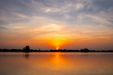 Akşamları güzel günbatımının manzarası gölün üzerinde, gölün üzerinde siluet suyun üzerinde ve bulutların sakin sularda yansıması.