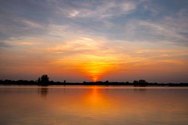 Akşamları güzel günbatımının manzarası gölün üzerinde, gölün üzerinde siluet suyun üzerinde ve bulutların sakin sularda yansıması.