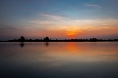 Akşamları güzel günbatımının manzarası gölün üzerinde, gölün üzerinde siluet suyun üzerinde ve bulutların sakin sularda yansıması.