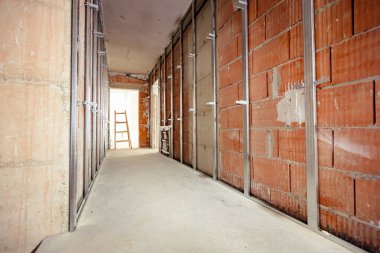 Uzun koridor boyunca bak, alçı duvarlar için monte edilmiş dikey metal profilleri olan koridor, inşaat halindeki tamamlanmamış konutların kapalı alanlarında çalışma devam ediyor. Mimari