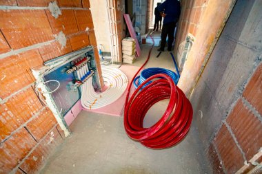 Yeni dağıtım sistemi yapım aşamasındaki bir binanın merkezi ısıtma katı için monte edildi. Beton zeminde kırmızı izole borular..