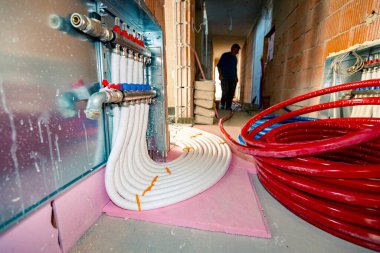 Yeni dağıtım sistemi yapım aşamasındaki bir binanın merkezi ısıtma katı için monte edildi. Beton zeminde kırmızı izole borular..