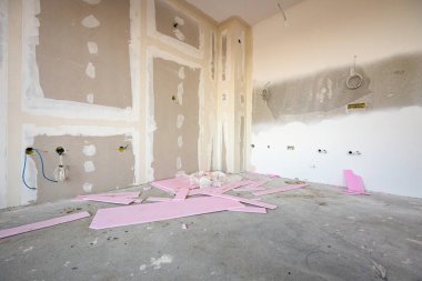 İnşaat alanında inşaat halindeki bölme duvarına elektrik kabloları ve delikleri olan kahverengi alçı tahtalarının ön görüntüsü. Pembe polistiren, köpük parçaları.