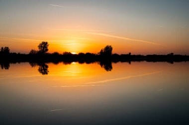 Akşamları güzel günbatımının manzarası gölün üzerinde, gölün üzerinde siluet suyun üzerinde ve bulutların sakin sularda yansıması.