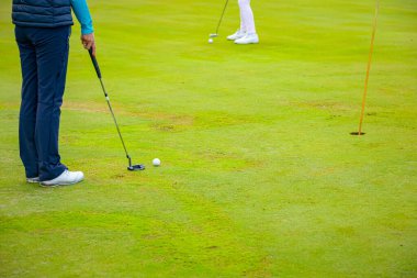 İnsanlar golf oynuyor, golf oynarken çim sahası, saha. Odaklanmış golfçü, topu deliğe, konsantrasyona ve hassasiyete sokmayı hedefleyen pitoresk bir golf sahası..