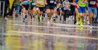 Büyük bir koşucu grubu, bir sokak maratonunda koşan sporcular, yağmurlu bir günde şehir yarışında koşan bir kalabalık..