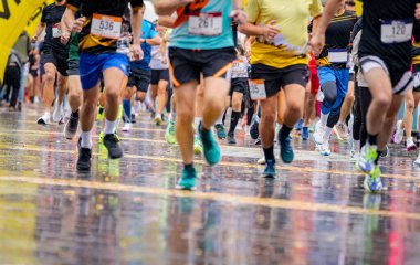 Büyük bir koşucu grubu, bir sokak maratonunda koşan sporcular, yağmurlu bir günde şehir yarışında koşan bir kalabalık..