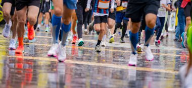 Büyük bir koşucu grubu, bir sokak maratonunda koşan sporcular, yağmurlu bir günde şehir yarışında koşan bir kalabalık..