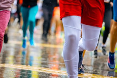 Ayakları ve bacakları düşük, büyük bir grup koşucu, atletler sokak maratonu yarışması, yağmurlu bir günde yarışan insan kalabalığı.