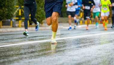 Ayakları ve bacakları düşük, büyük bir grup koşucu, atletler sokak maratonu yarışması, yağmurlu bir günde yarışan insan kalabalığı.