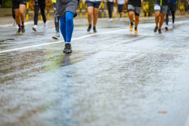 Ayakları ve bacakları düşük, büyük bir grup koşucu, atletler sokak maratonu yarışması, yağmurlu bir günde yarışan insan kalabalığı.