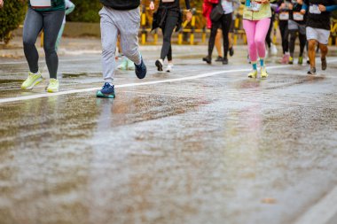 Ayakları ve bacakları düşük, büyük bir grup koşucu, atletler sokak maratonu yarışması, yağmurlu bir günde yarışan insan kalabalığı.