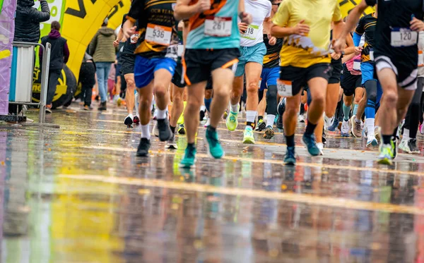 Büyük bir koşucu grubu, bir sokak maratonunda koşan sporcular, yağmurlu bir günde şehir yarışında koşan bir kalabalık..