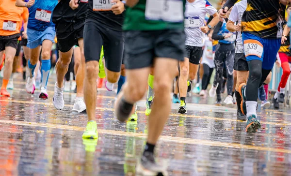 Büyük bir koşucu grubu, bir sokak maratonunda koşan sporcular, yağmurlu bir günde şehir yarışında koşan bir kalabalık..