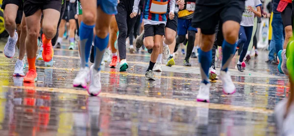Büyük bir koşucu grubu, bir sokak maratonunda koşan sporcular, yağmurlu bir günde şehir yarışında koşan bir kalabalık..