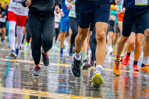 Ayakları ve bacakları düşük, büyük bir grup koşucu, atletler sokak maratonu yarışması, yağmurlu bir günde yarışan insan kalabalığı.