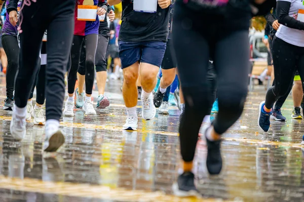 Ayakları ve bacakları düşük, büyük bir grup koşucu, atletler sokak maratonu yarışması, yağmurlu bir günde yarışan insan kalabalığı.