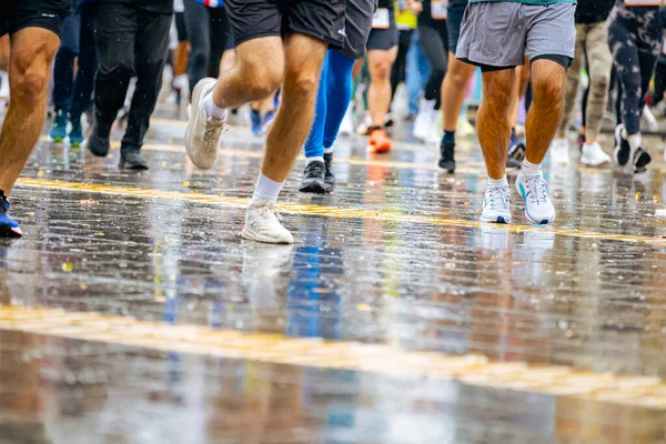 Ayakları ve bacakları düşük, büyük bir grup koşucu, atletler sokak maratonu yarışması, yağmurlu bir günde yarışan insan kalabalığı.