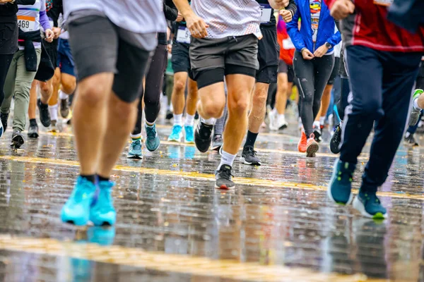 Ayakları ve bacakları düşük, büyük bir grup koşucu, atletler sokak maratonu yarışması, yağmurlu bir günde yarışan insan kalabalığı.
