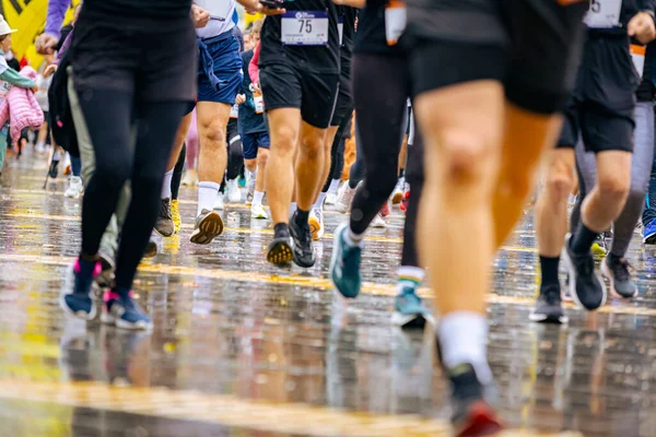Ayakları ve bacakları düşük, büyük bir grup koşucu, atletler sokak maratonu yarışması, yağmurlu bir günde yarışan insan kalabalığı.