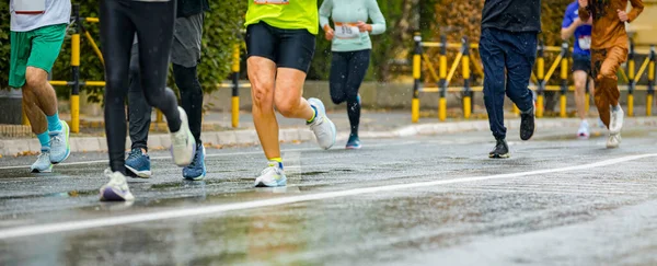 Ayakları ve bacakları düşük, büyük bir grup koşucu, atletler sokak maratonu yarışması, yağmurlu bir günde yarışan insan kalabalığı.