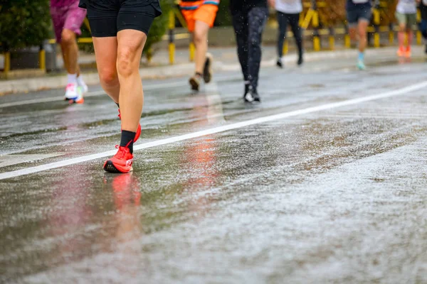 Ayakları ve bacakları düşük, büyük bir grup koşucu, atletler sokak maratonu yarışması, yağmurlu bir günde yarışan insan kalabalığı.