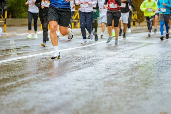 Ayakları ve bacakları düşük, büyük bir grup koşucu, atletler sokak maratonu yarışması, yağmurlu bir günde yarışan insan kalabalığı.