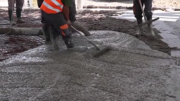 Los trabajadores están esparciendo hormigón sobre un gran piso reforzado en el sitio de construcción . — Vídeos de Stock