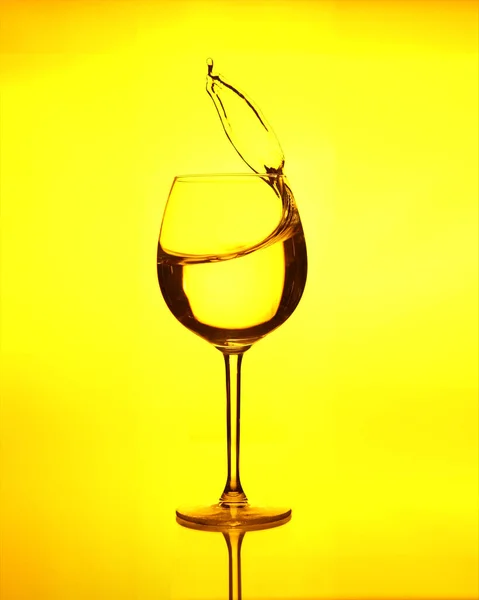 Water splash in a wine glass on yellow background