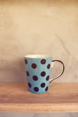 Ahşap arka plan ve çimento duvar üzerinde noktalı pastel mavi Kupası.