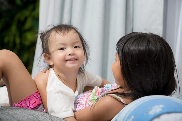 自宅のベッドに彼女の妹と遊ぶかわいいアジアの女の子. — ストック写真