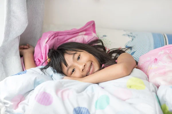 Aziatische meisje onder een deken in het bed liggen en glimlachen — Stockfoto