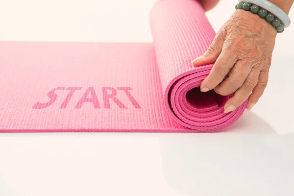 Senior hand\'s rolling pink yoga mat on white with message start