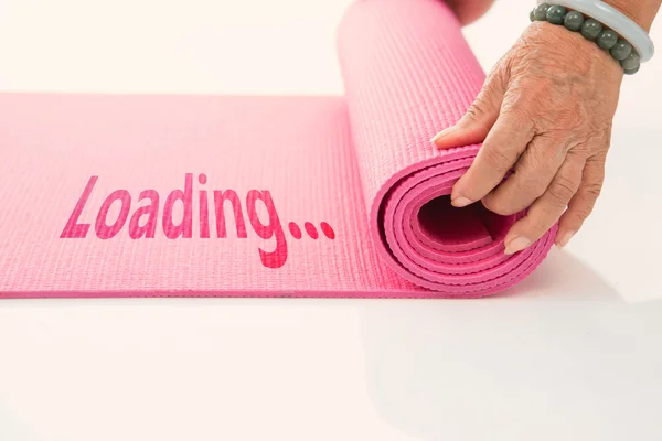 Старший рука катит розовый циновку йоги на белом с сообщением нагрузки — стоковое фото