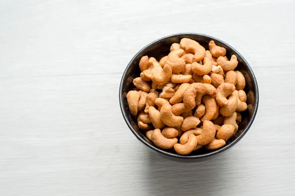 Salty cashew nuts in black ceramic bowl on gray wood table — Stock Photo, Image