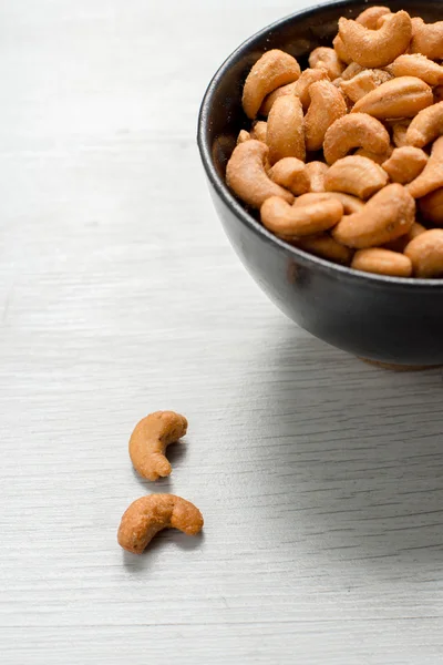 Salty cashew nuts in black ceramic bowl on gray wood table — Stock Photo, Image