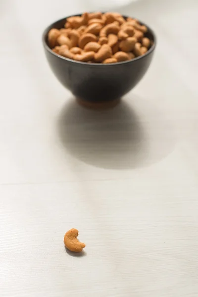 Salty cashew nuts in black ceramic bowl on gray wood table — Stock Photo, Image