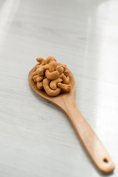 Anacardos salados en cuchara de madera sobre mesa de madera gris — Foto de Stock