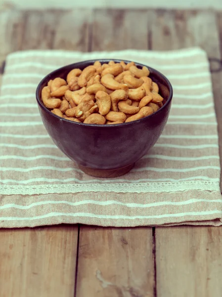 Salty cashew nuts in black ceramic bowl on wood table — Stock Photo, Image