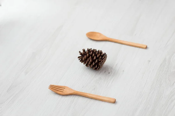 Dennenappel met vork en lepel op grijs houten tafel. — Stockfoto
