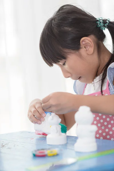 Asian child paints the colors of white plaster doll toys on the — Stock Photo, Image