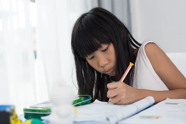 Bonito ásia menina escrevendo lição de casa em um livro em casa — Fotografia de Stock