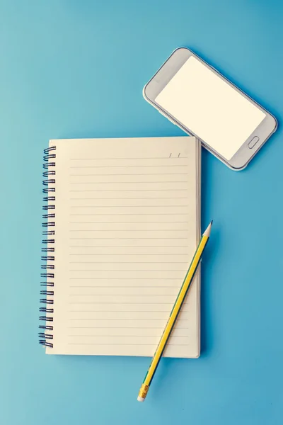 Matita e blocco note Smart Phone su sfondo blu . — Foto Stock
