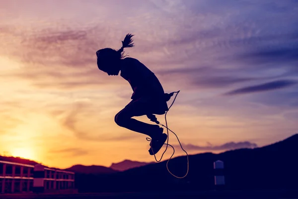 Menina pulando corda em silhueta com pôr do sol — Fotografia de Stock