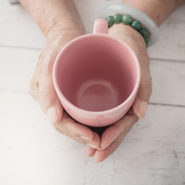 Senior hält eine rosa leere Tasse auf weißem Holzgrund — Stockfoto