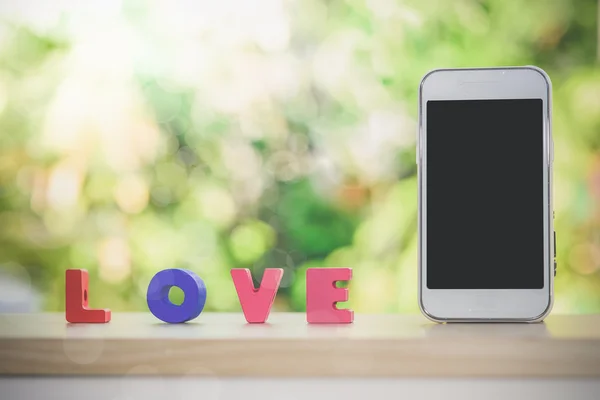 Smart phone and love alphabet on wood with bokeh background, — Stock Photo, Image