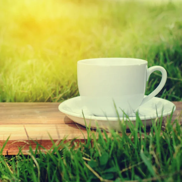 Lege koffie beker op een houten bord met gras en natuurlijk licht. — Stockfoto