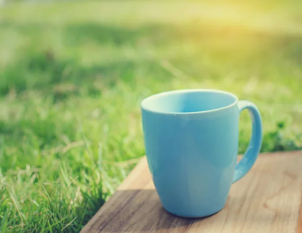 Blauer Becher auf Holzbrett mit grünem Rasenplatz. — Stockfoto